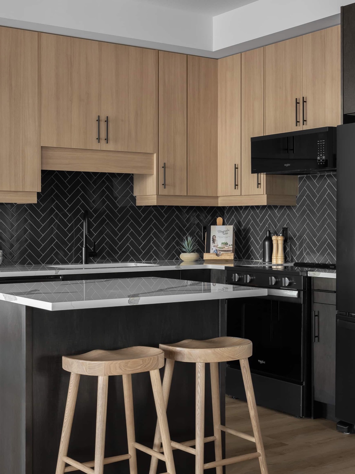Two-tone kitchen with light-oak upper cabinets and black island in a decorated model home